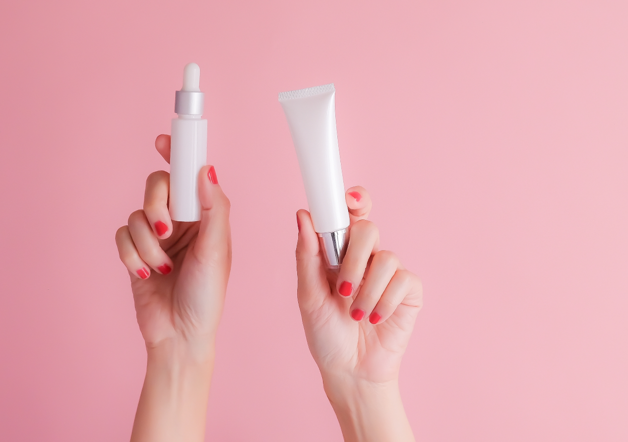 Woman's Hands with a Tube of Cream and a Face Serum while is Wearing Red Nail Polish