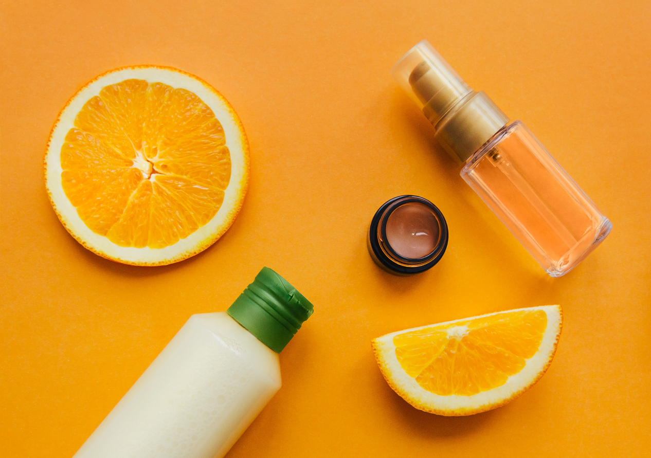 Skincare Products for Treating Dark Circles on a Orange Background and Some Orange Slices Next to them
