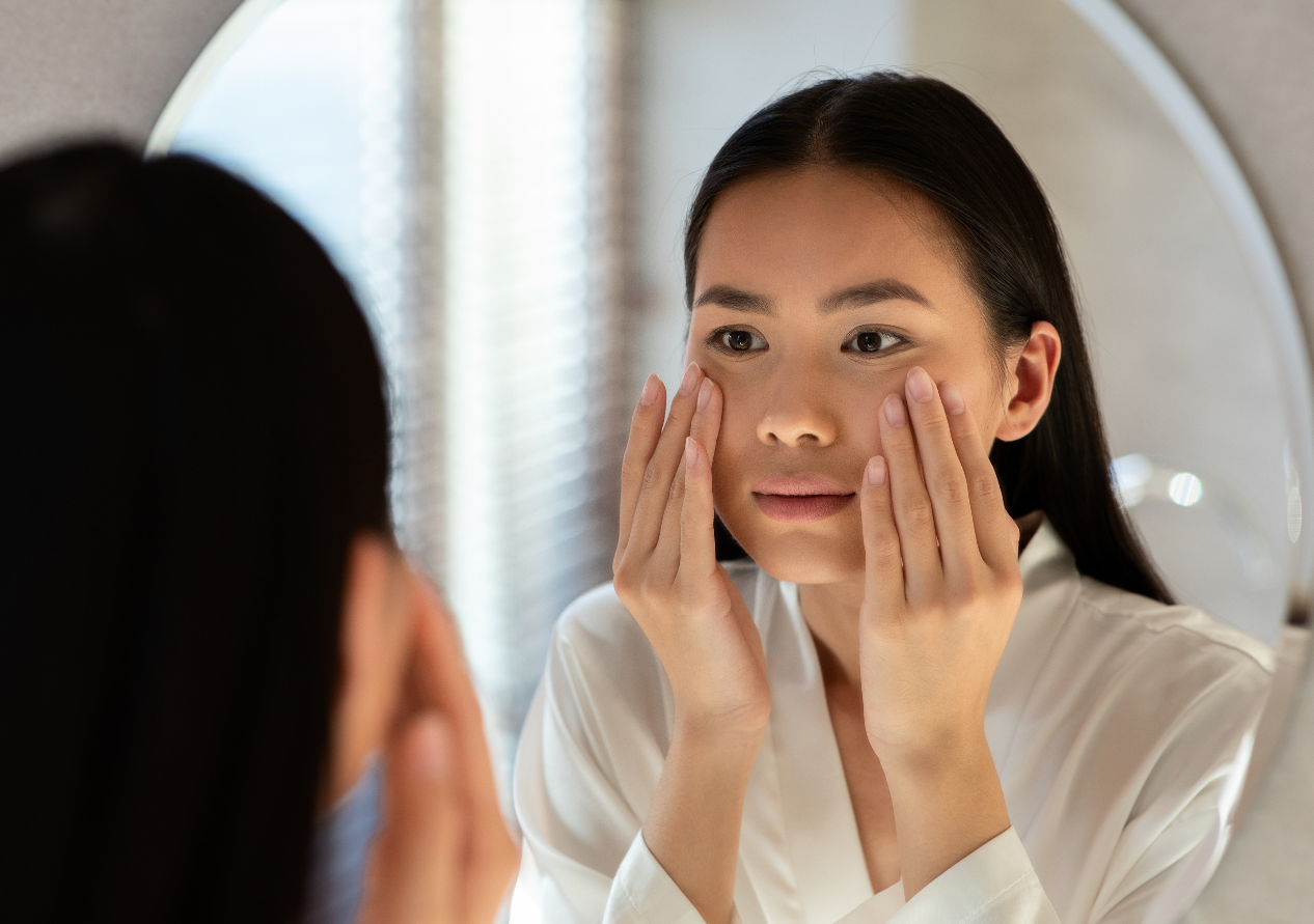 Asian Young Woman Looking her at the Mirror while Touching her Face