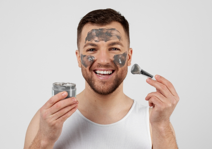 Happy Young Man Robbing Facial Mask on Face